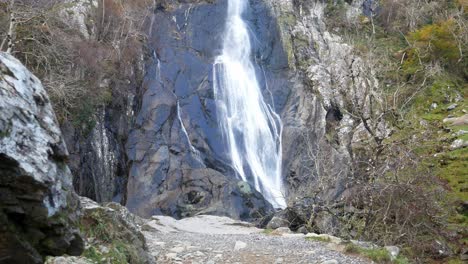 Felsiger-Kaskadierender-Wasserfall,-Der-Direkt-Hinter-Felsbrocken-In-Gezackte-Flussfelsen-Stürzt