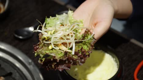 Person-Making-Lettuce-Leaf-Ssam---Korean-Pork-Belly-Barbecue-Wrapped-In-Lettuce-With-Ssamjang