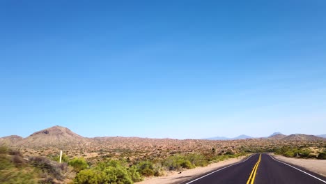 POV-driving-through-the-flat-land-of-the-Sonoran-Desert-toward-a-distant-mountain-ridge,-Scottsdale,-Arizona