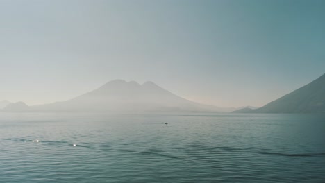 Drone-aerial-view,-a-man-on-a-boat-on-Lake-Atitlan-and-volcanoes-surrounding-it-in-lake-Atitlan,-Guatemala