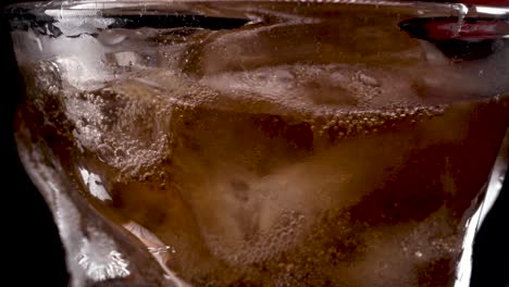 Cola-and-ice-in-glass,-Cola-pouring-into-a-curvy-glass-with-ice-cubes