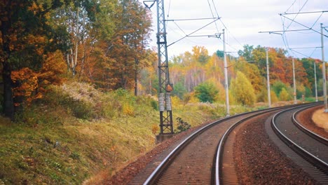 Blick-Hinter-Einen-Zug-An-Einem-Schönen-Herbsttag,-Während-Er-Die-Eisenbahn-Hinunterfährt-Und-Herbstblätter-Von-Den-Bäumen-Fallen