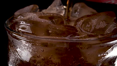 Cola-and-ice-in-glass,-Cola-pouring-into-a-curvy-glass-with-rising-ice-cubes