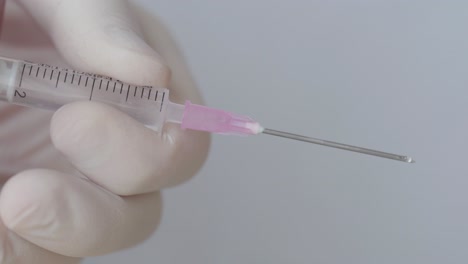 Droplets-On-Hypodermic-Syringe-While-Pressing-With-Hand-In-Surgical-Glove,-Close-Up-Shot