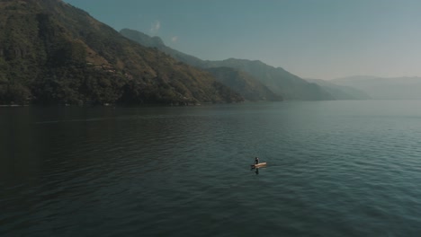 Drone-aerial-rotating-around-a-man-on-a-boat-during-beautiful-sunrise-in-lake-Atitlan,-Guatemala