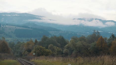Railroad-tracks-cutting-it´s-way-through-a-forest-with-amazing-view-of-surrounding-lanscape-covered-in-haze-and-white-clouds,-Slovakia,-Horehronský-expres,-banska-bystrica