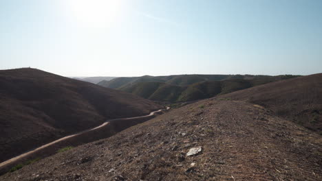 Dirt-trails-and-barren-hills-in-the-harsh-landscape-of-Algarve-Portugal---Tilt-up-Reveal-shot