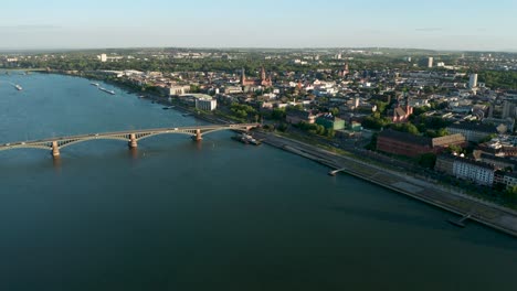 Drone-flight-over-the-city-of-Mainz-where-Biontech-was-founded-during-daylight-with-green-trees,-the-old-bridge-and-the-red-Dome-in-the-Background