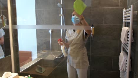 Ein-Zimmermädchen-Mit-Gesichtsmaske-Reinigt-Und-Desinfiziert-Die-Dusche-Eines-Hotelzimmers