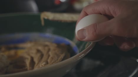 Hand-Breaking-Egg-In-A-Bowl-With-Cookie-Dough-Mixture---close-up