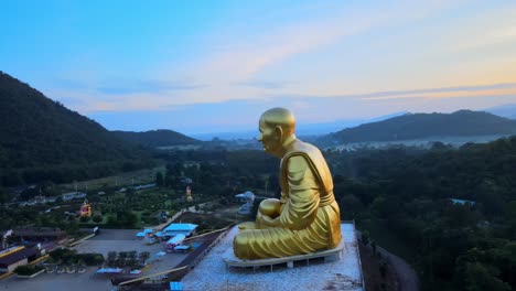 4k-360-around-Aerial-drone-footage-of-a-huge-golden-monk-statue-surrounded-by-mountains-of-Khao-Yai-at-dusk-in-Thailand