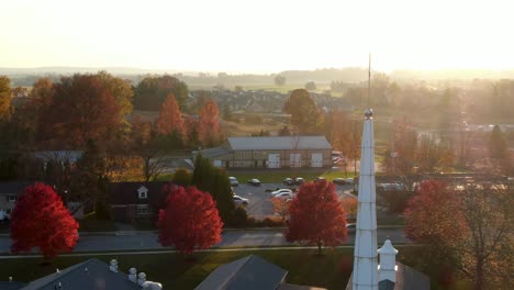 Aerial-of-Christian-Church-steeple-during-dramatic-sunset,-sunrise-in-small-town-in-America