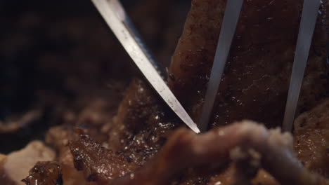 Fork-holds-juicy-meat-in-place-for-scissors-to-cut-portion,-close-up