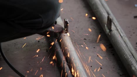 Remove-excess-weld-metal-in-iron-pipes-and-get-the-smooth-finishing-of-the-welding,-using-electric-hand-grinder-by-the-handyman-outdoor-slow-motion-clip,-sparkes-of-particles-coming-towards-the-camera