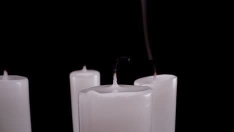 macro-close-up-extinguishing-white-burning-candles-on-black-background,-4k-footage