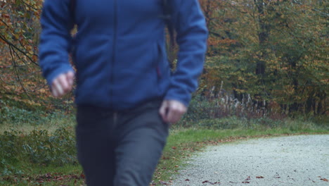 Man-with-backpack-runs-past-camera-along-autumn-trail,-slow-motion