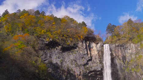 Mittlere-Aufnahme-Eines-Wasserfalls,-Der-Von-Hohen-Felsen-Mit-Herbstfarben-An-Der-Spitze-Fällt