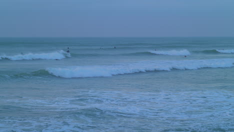 Surfers-ride-ocean-waves-during-blue-hour,-slow-motion