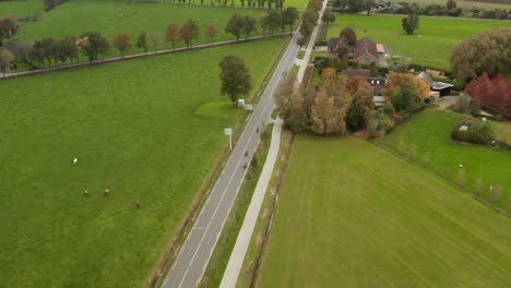 High-drone-shot-of-three-motorbikes-riding-through-lush,-green-grass,-dutch-landscape-on-paved-road