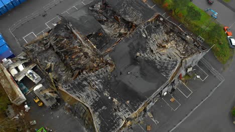 Aerial-view-of-damaged-warehouse-building-with-burnt-roof,-zoom-out