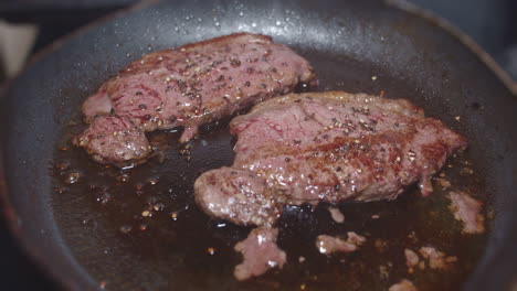 Thin-steaks-cooking-in-oil-in-skillet-and-being-turned-with-spatula