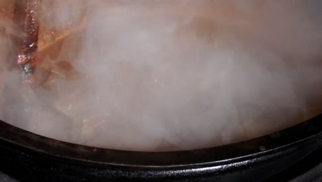Close-up-view-of-steaming-hot-meat-stew-being-stirred-with-a-wooden-spoon-in-a-large-copper-pot,-SLOW-MOTION