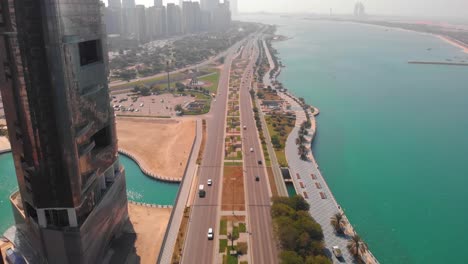 Luftaufnahme-Nach-Unten-Auf-Eine-Autobahn-In-Abu-Dhabi-Zwischen-Den-Wolkenkratzern-Und-Dem-Wasser