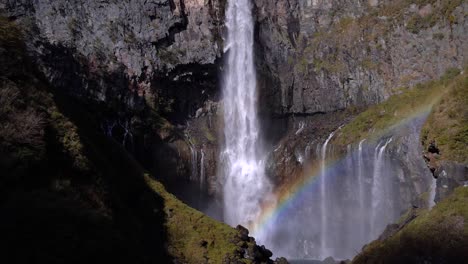 Tilt-down-over-beautiful-high-waterfall-falling-from-rocks-with-rainbow