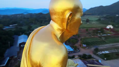 4k-Luftaufnahme-Aus-Der-Nähe-Einer-Größten-Luang-Pu-Thuat-Goldenen-Statue-Der-Welt,-Umgeben-Von-Bergen-Von-Khao-Yai-Im-Morgengrauen-In-Thailand