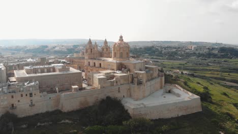 Mdina-city-outside-city-walls,-revealing-the-Cathedral-of-Saint-Paul---Low-angle-point-of-interest-Aerial-shot