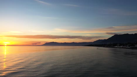 Sonnenuntergang-Blick-Auf-Das-Meer-Von-Marbella-Bei-Sonnenuntergang,-Aufnahme-Mit-Gimbal-Auf-Einem-Boot,-Das-Sich-Zum-Mittelmeer-Bewegt-Paddelsurfer-In-Der-Ferne