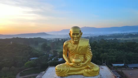 4k-Antena-Gran-Estatua-De-Monje-Luang-Por-Tuad-Rodeada-De-Montañas-De-Khao-Yai-Al-Amanecer-En-Tailandia