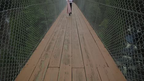 Young-Woman-Walks-Across-Suspended-Footbridge-In-Coaticook,-Eastern-Townships,-Quebec-Canada,-Tilt-Up,-Full-Body-Shot,-Slow-Motion