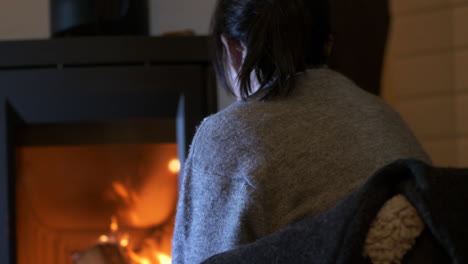 Close-view-from-behind-of-woman-sitting-by-wood-burning-stove-indoors