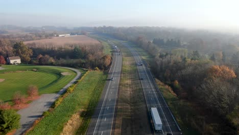 Aerial-dolly-shot-above-two-lane-divided-highway-in-United-States-of-America,-USA-during-foggy-bright-autumn-day