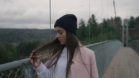 Attractive-Lady-Stroking-Her-Long-Hair-While-Walking-On-Bridge-During-Winter-In-Coaticook,-Quebec-Canada,-Slow-Motion-Shot