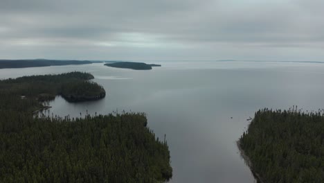Aerial-shot-over-a-huge-lake-and-forest-on-a-cloudy-day-showing-a-small-isolated-cabin