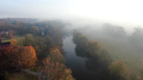 Beautiful-cinematic-aerial-of-autumn-trees-by-quiet-river-during-foggy-morning