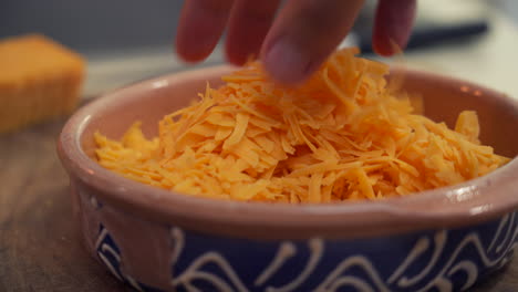 Chef-hand-mixing-a-freshly-grated-pile-of-cheddar-cheese