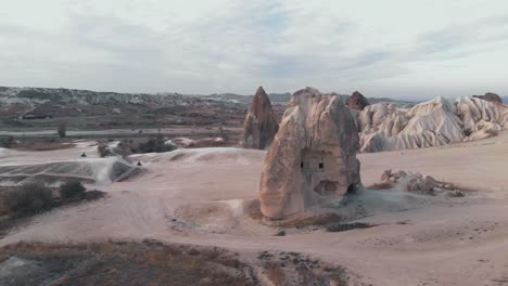 Barren-landscape-with-Soaring-rock-formation-with-Traditional-house-in-Cappadocia,-Turkey---Low-Angle-Orbit-Aerial