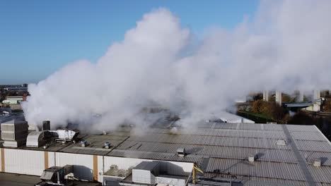 Wide-shot-thick-industrial-smoke-bellows-from-chimney-above-warehouse