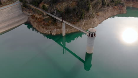 Die-Drohne-Umkreist-Einen-Turm,-Der-An-Einem-Damm-Befestigt-Ist,-Der-In-Türkisfarbenes-Reservoirwasser-Getaucht-Ist