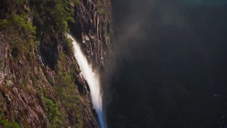Static-view-of-Ellenborough-falls-in-Australia,-water-flowing-off-the-cliff-edge-with-haze-and-mist-lit-by-golden-hour-light