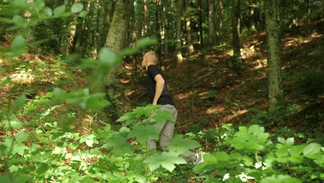 Fit-young-man-walking-in-forest-in-summer,-defocus-grom-green-leaf