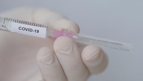 Attaching-Hypodermic-Needle-With-Plastic-Cap-To-Syringe-With-Fluid-And-Covid-19-Label---close-up