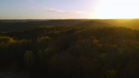 Aerial-flight-over-beautiful-autumn-forest-in-rolling-rural-hilly-countryside-at-sunset