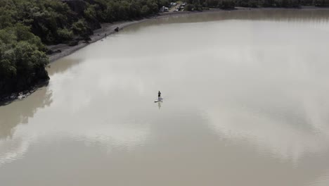 Man-on-standup-paddle-board-floating-on-cold-water-of-Lagarfljot-lake,-aerial