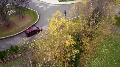 Overhead-aerial-of-autumn-trees-and-a-tilt-up-to-a-red-minivan-pulling-into-a-church-parking-lot-in-Lafayette-Hill,-PA