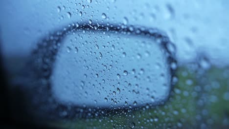 Raindrops-on-passenger-seat-window-with-mirror-during-bad-weather,-focus-pull