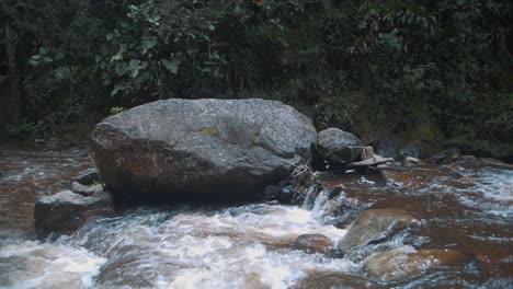 Water-flowing-through-a-river-with-rocks-in-slow-motion-in-Cocora-Valley,-Colombia